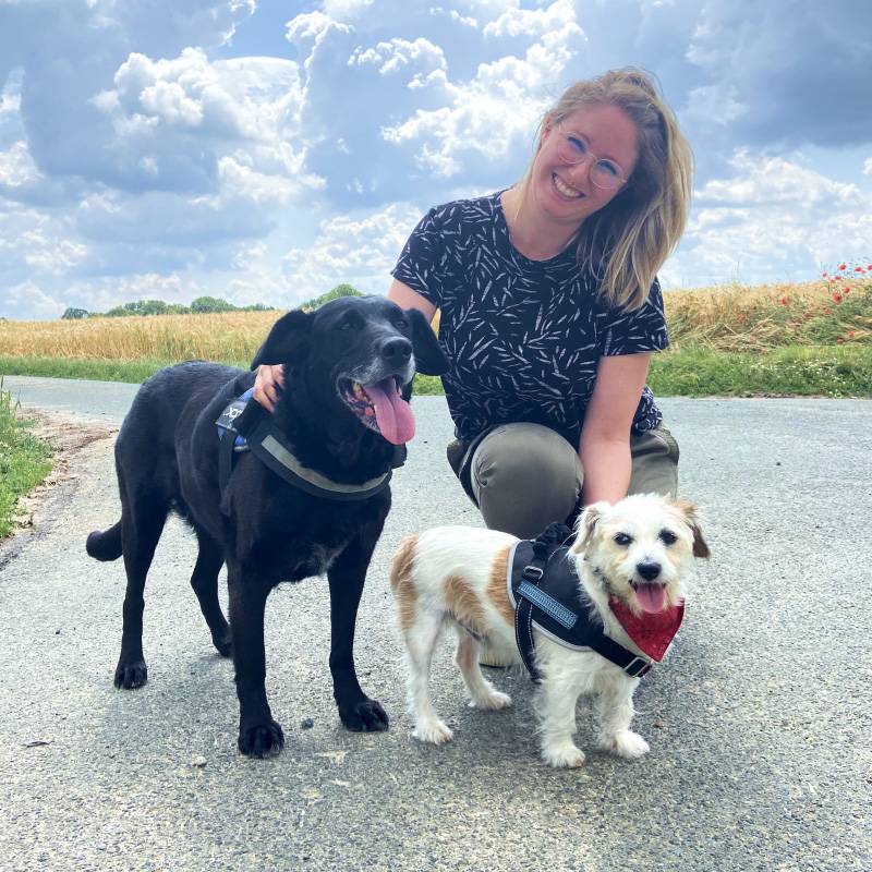 Julia Inhaberin von Pfötchenheldin sitzt mit zwei Hunden auf einem Weg und lächelt in die Kamera